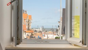 Blick aus einem Fenster auf eine Straße mit Gebäuden, einem klaren Himmel und ein Wasser im Hintergrund.