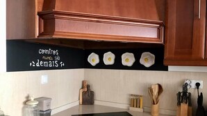 A kitchen with wooden cabinets, a black stovetop, and a backsplash with a black sign. - Charming 5-bed House in Granja (Mourão)