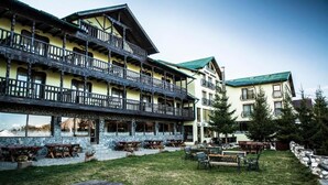 A multi-story building with outdoor seating areas and a stone facade. - Pensiunea Padina Ursului (Fundata)