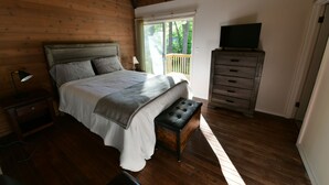 A bedroom with a wooden ceiling, a bed with a grey headboard, a bench, a dresser, and a television on a stand. - Spacious, renovated 3 bedroom home in Traverse City (Traverse City)