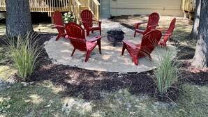 A backyard with a fire pit, red Adirondack chairs, and a covered deck area. - Spacious, renovated 3 bedroom home in Traverse City (Traverse City)
