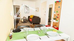 Un coin repas avec une table blanche dressée pour deux personnes, un chemin de table vert et un mur en bois orné de boules colorées.