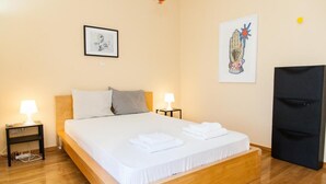 Un lit bien fait, avec du linge de lit et des serviettes blanches, deux lampes de chevet, une œuvre d’art encadrée au-dessus du lit et une armoire noire sur le côté droit.