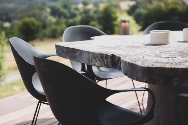 A wooden table with chairs on a deck, overlooking a green landscape.