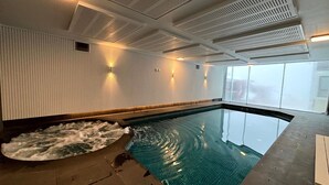 A swimming pool with a textured wall and ceiling vents, a clear view of the sky, and a tiled floor.