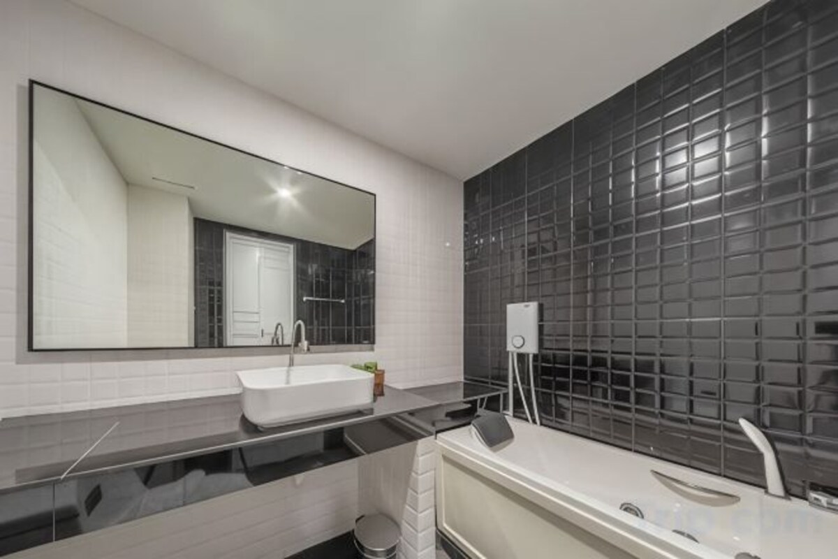 Un baño moderno con un espejo grande, un lavamanos blanco y una pared de azulejos negros.