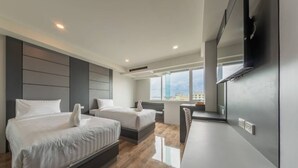 A modern hotel room with two beds, a desk, and a large window offering a city view. - The Ring Border (Sadao)