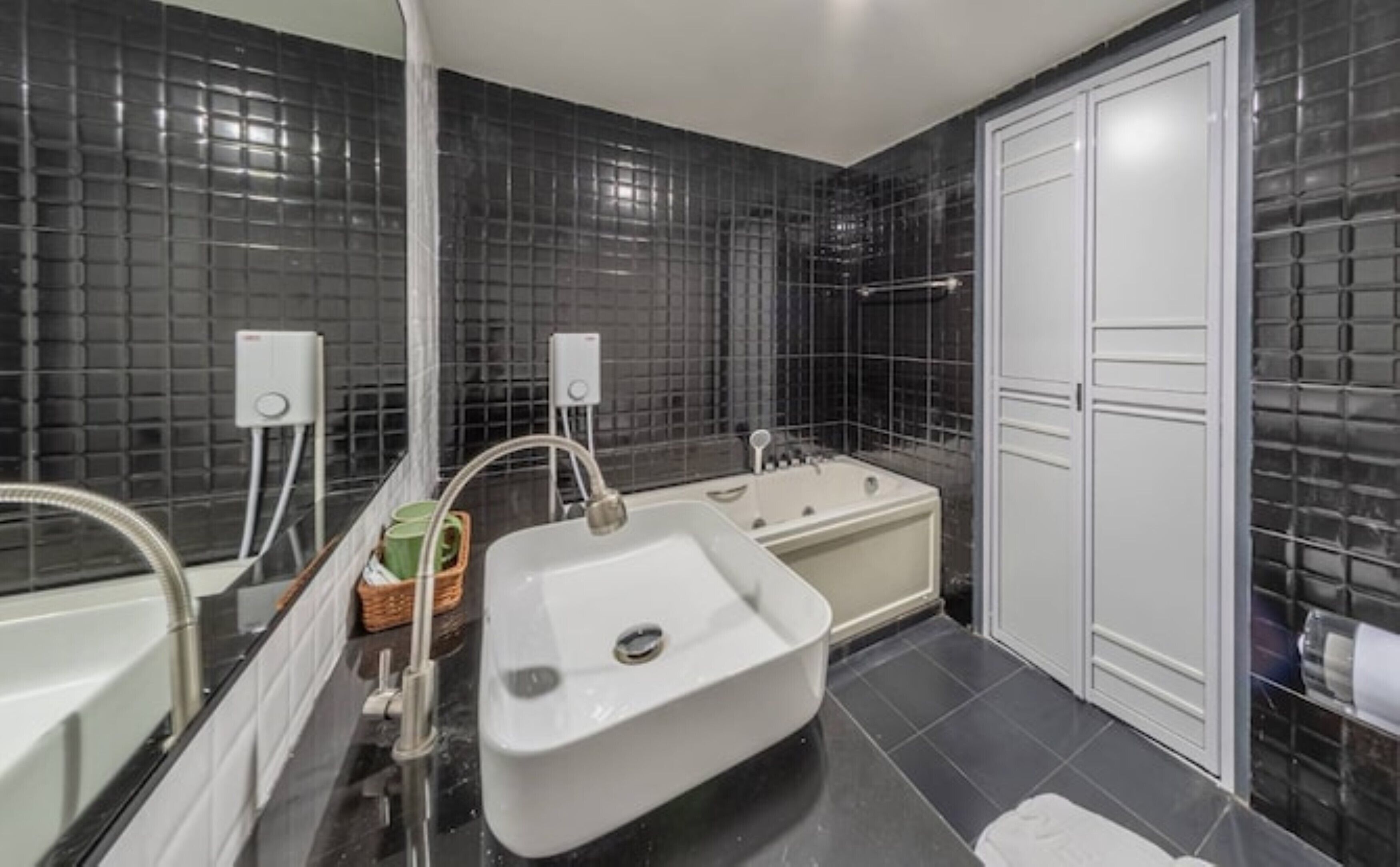 A modern bathroom with a white sink, a bathtub, and a white door.