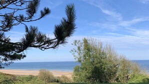 Un mur de pierre, une zone herbeuse et une vue sur la plage et l’océan.