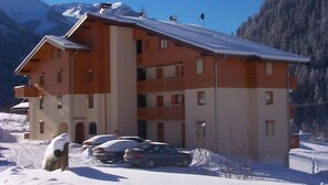 A multi-story building with a sloped roof, likely a hotel or apartment complex, surrounded by snow and mountains in the background. - Bright apartment for 6 people with balcony and parking in Châtel (Châtel)