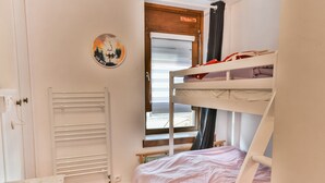 Quarto com beliches, um radiador, uma janela com cortinas e um quadro fixado na parede.