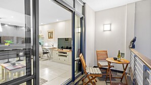 A modern interior with a balcony, a dining area with wooden chairs and a small table, and a kitchen in the background. - Eden on the Bay 150 by HostAgents (Cape Town)