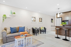 A modern living room with a sofa, two armchairs, a coffee table, and a kitchen area with a bar. - Eden on the Bay 150 by HostAgents (Cape Town)