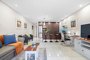Uma sala de estar moderna com sofá, mesa de centro e área de cozinha com mesa de jantar e banquetas.