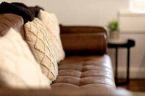 Un canapé en cuir marron, agrémenté d’un plaid texturé et d’un coussin.