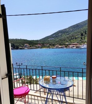 A balcony with a glass table and chairs, overlooking a body of water and a hillside with buildings. - Fabulous apt. w breakfast near the sea (Lefkada)