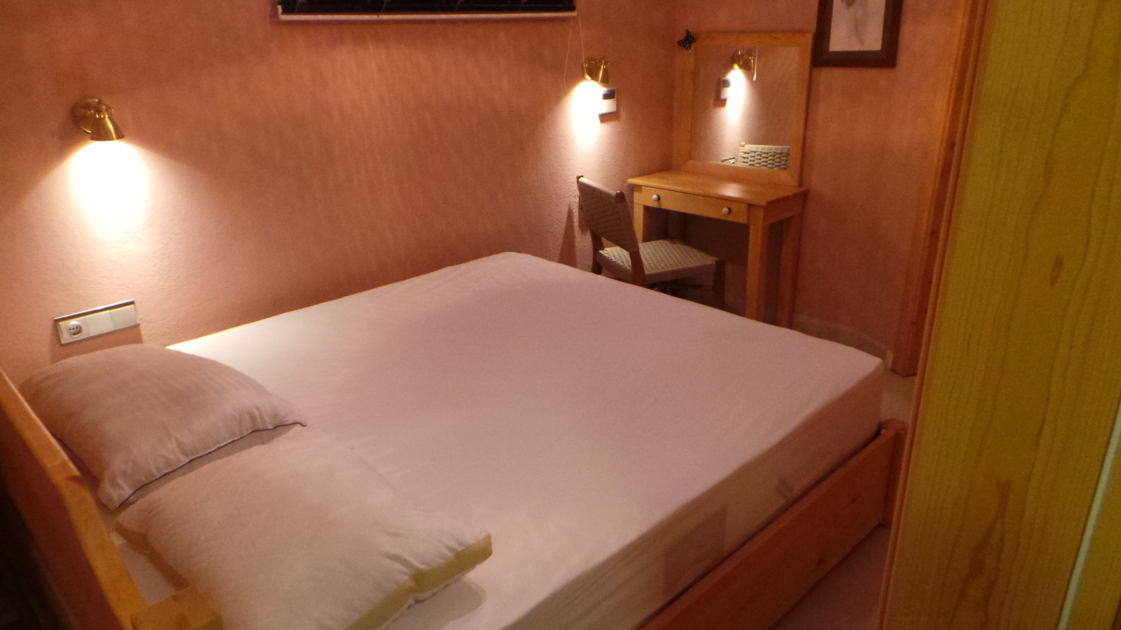 A bedroom with a single bed, a wooden desk, a chair, and two wall-mounted lights.
