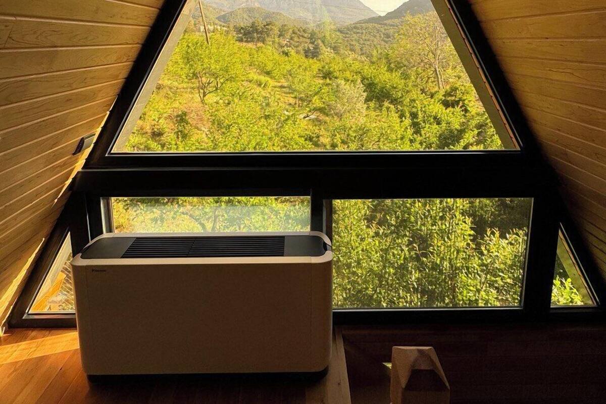 A triangular attic room with a view of green hills and mountains.