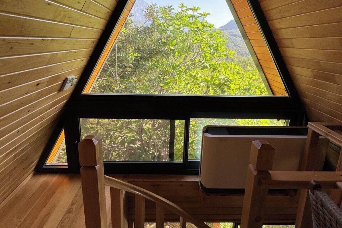 A wooden interior with a triangular skylight, a wooden chair, and a view of greenery outside.