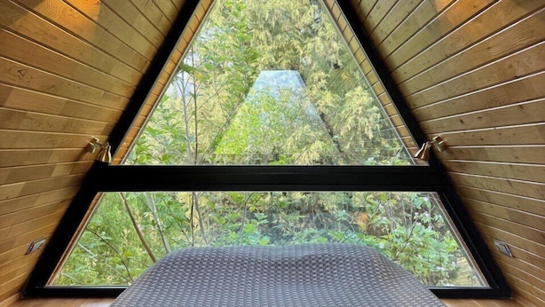 Ein raumförmiger, dreieckiger Raum mit Holzwänden und einem Schachbrettmuster-Boden, mit einem großen Dachfenster und zwei Wandleuchten.