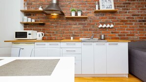 A modern kitchen with white cabinets, a brick wall, and a wooden countertop. - Air-conditioned Apartment in the Center | Separate Bedroom (Warszawa)