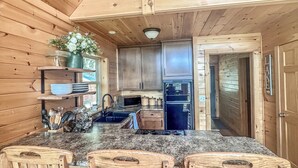 A wooden cabin interior with a kitchen featuring granite countertops, wooden chairs, and a dining table.