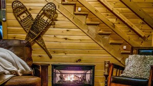 A cozy cabin interior with a wooden staircase, a fireplace, and a large wooden wall hanging.