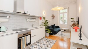 Una cucina moderna con pensili bianchi, forno integrato e macchina del caffè. C'è un'area pranzo con un divano scuro e un tavolino.