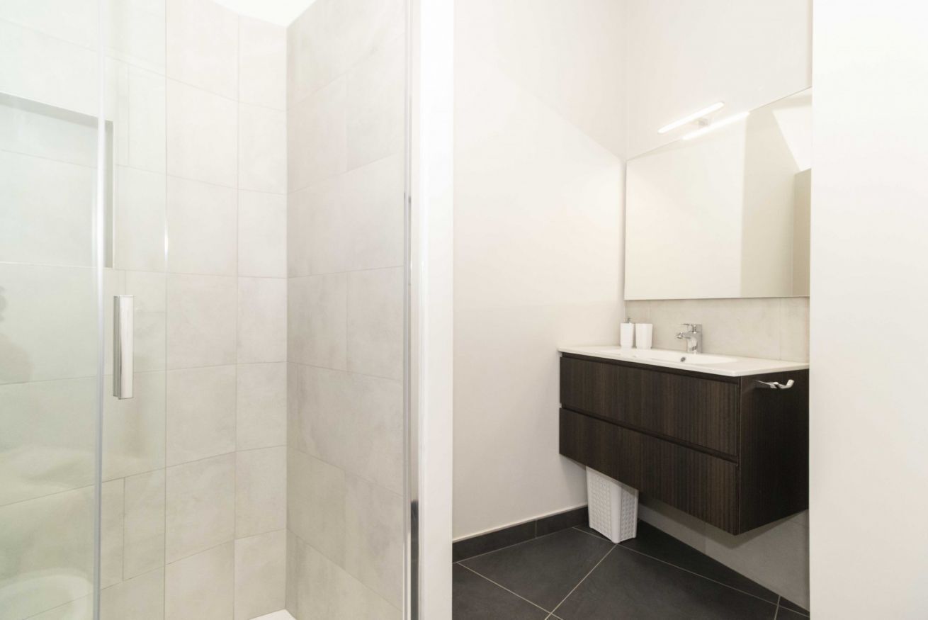 Een moderne badkamer met een douchecabine van glas, een donker houten wastafelmeubel en een grote spiegel.