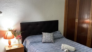 A bedroom with a bed, a nightstand, a lamp, a vase with flowers, and a wardrobe. - Studio in the center of Granada (Granada)