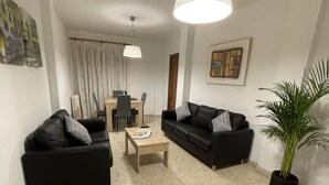 A living room with two black sofas, a wooden coffee table, a dining table with chairs, a potted plant, and a ceiling light. - Studio in the center of Granada (Granada)