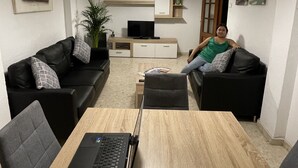 A modern living room with a wooden dining table, two black sofas, a laptop, a TV, and a hanging light fixture. - Studio in the center of Granada (Granada)