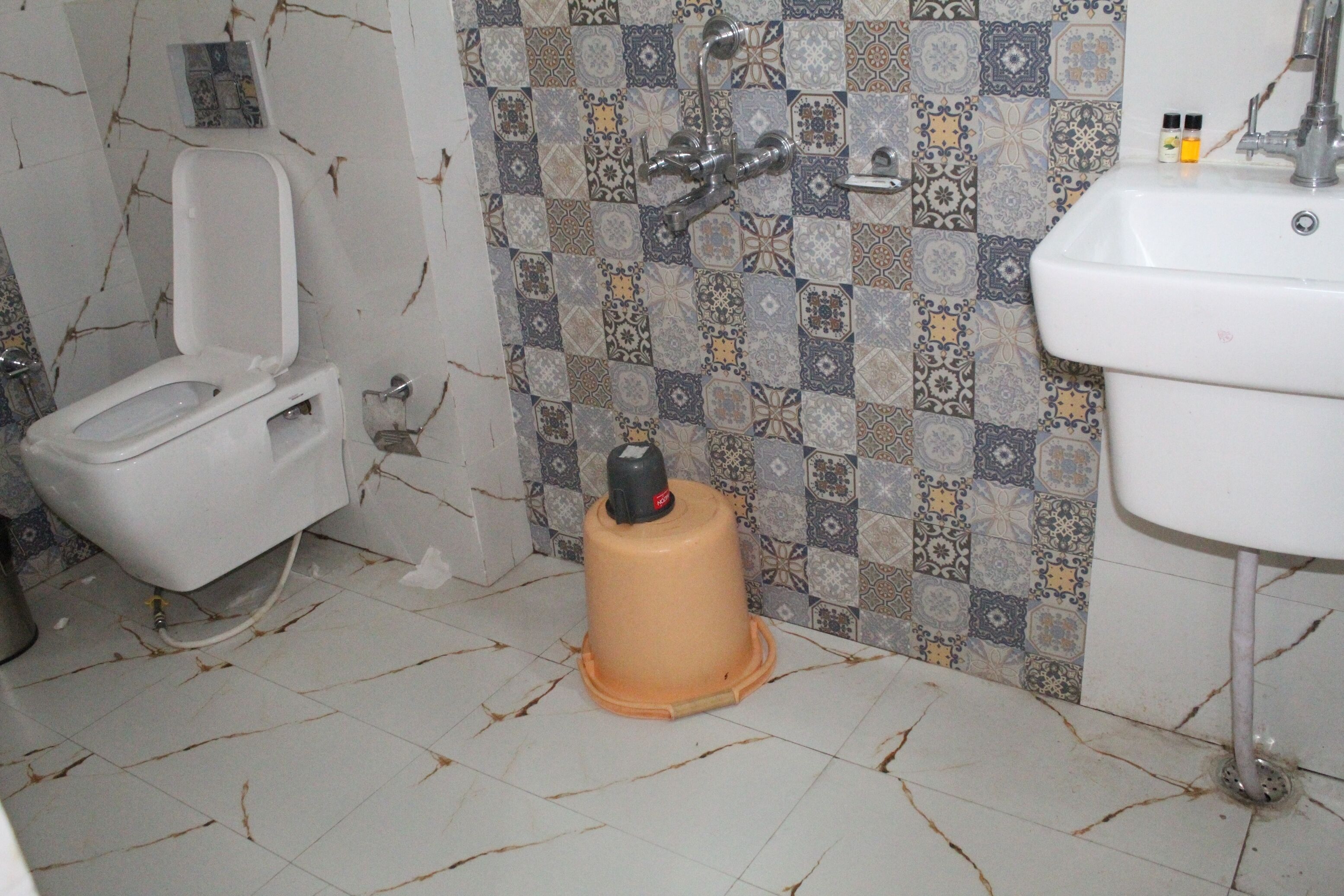A bathroom with a toilet, bidet, sink, and patterned tiles.