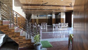 A spacious lobby with a staircase, ceiling fans, and a seating area with chairs. - Jalal Palace (Almora)