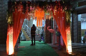 An indoor venue with a green carpet, red drapes, and floral decorations. - Jalal Palace (Almora)