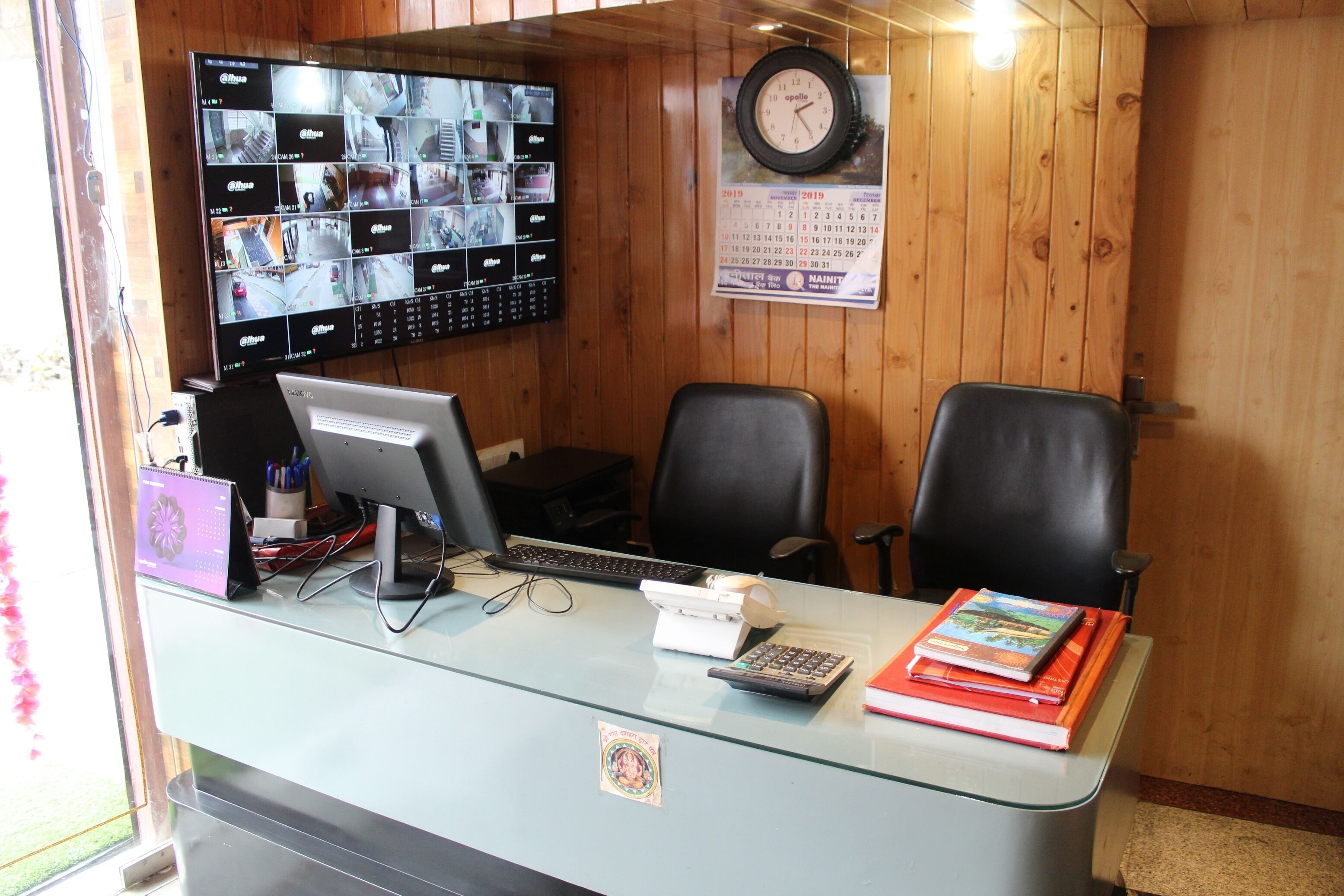 Una mesa de recepción con un monitor de computadora, dos sillas, un calendario y un reloj en la pared.