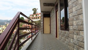 A stone-walled corridor with a wooden door, a metal railing, and a view of colorful buildings in the background. - Jalal Palace (Almora)