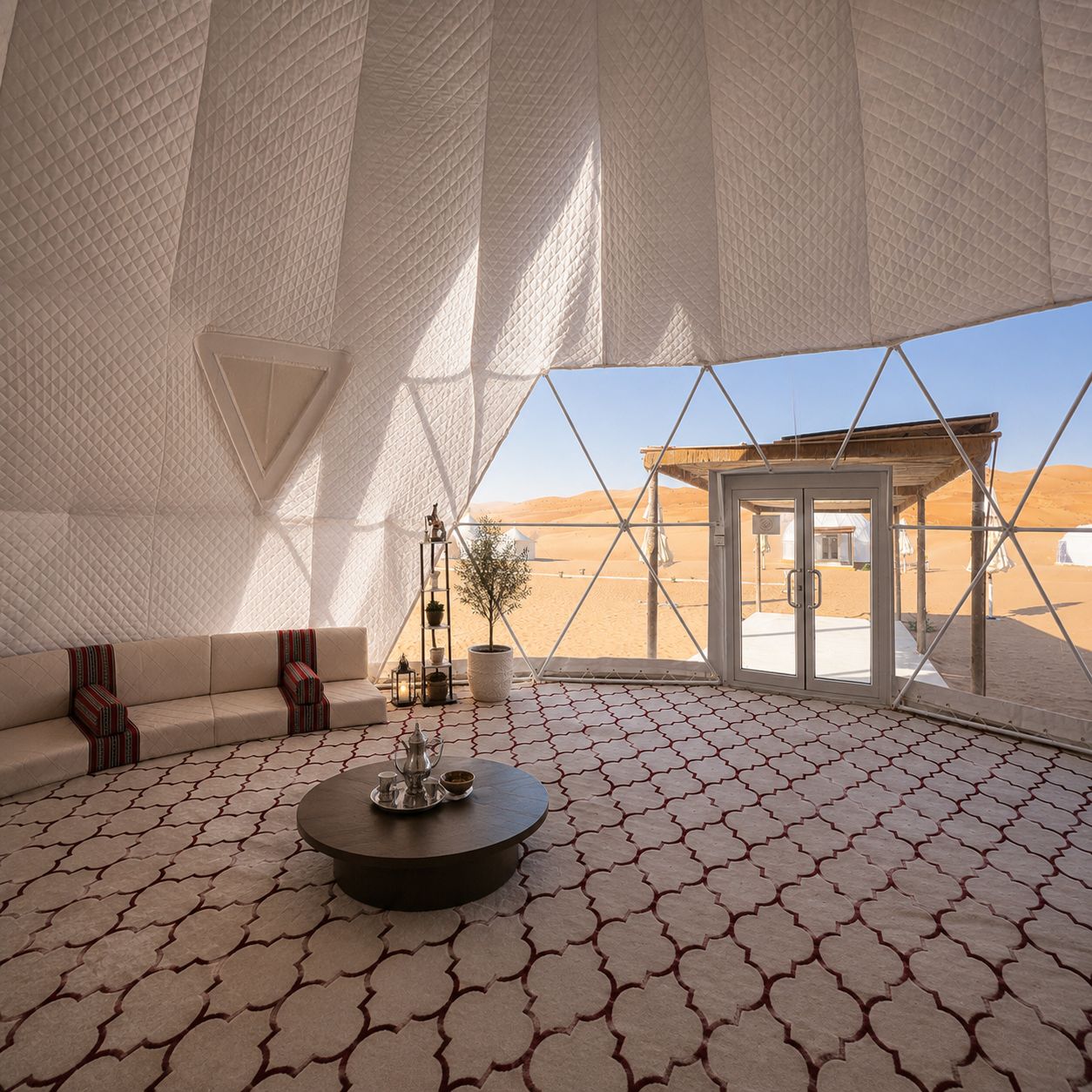 A tented room with a patterned floor, a sofa, a coffee table, and a view of the desert landscape.