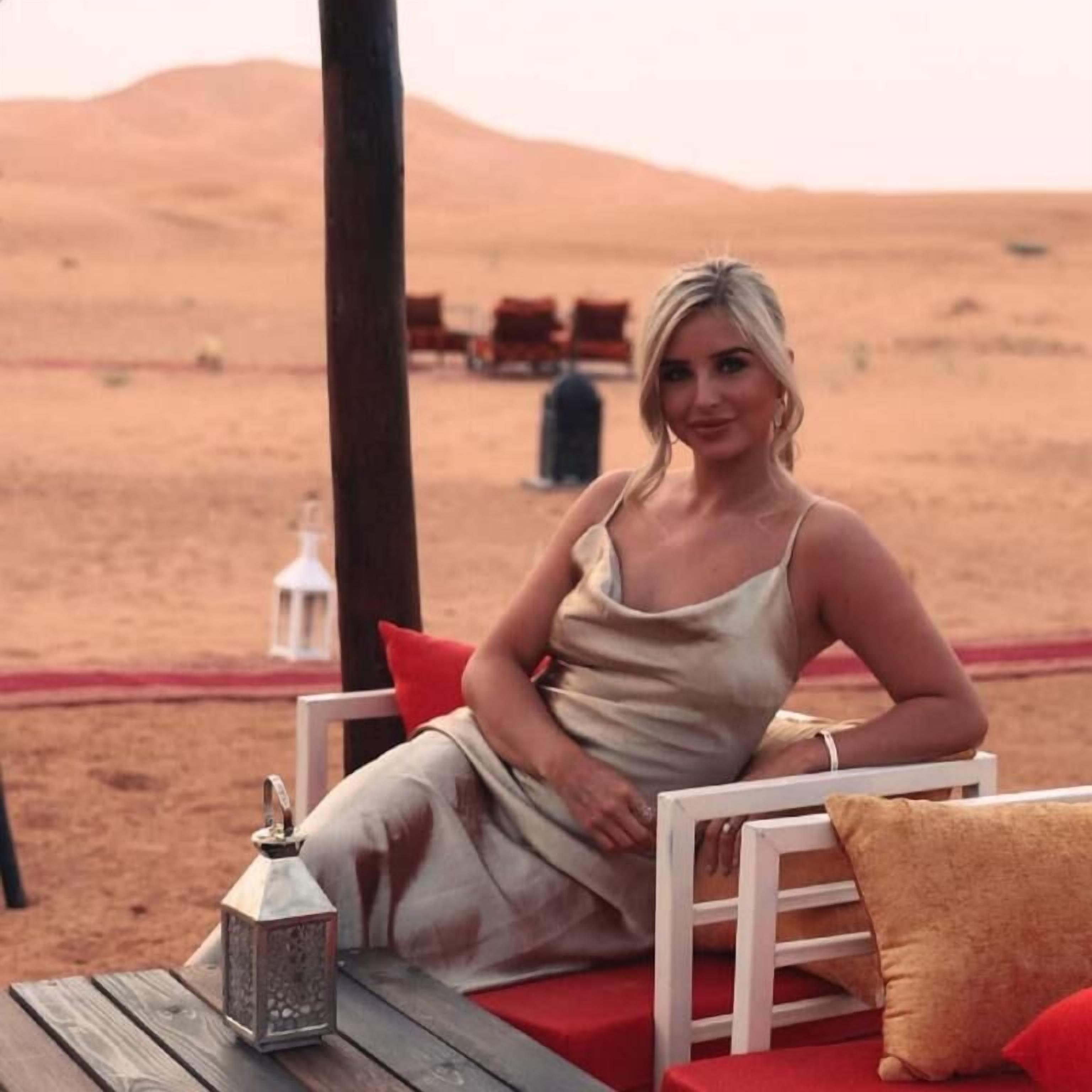 Un décor désertique avec une terrasse en bois, une chaise blanche et un coussin rouge.