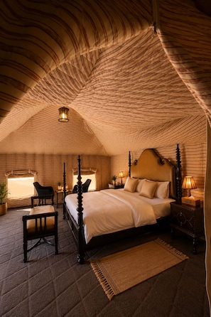 A bedroom with a four-poster bed, a nightstand with a lamp, a chair, and a window with a view. - Luxury Desert Camp Oman (Bidiya)