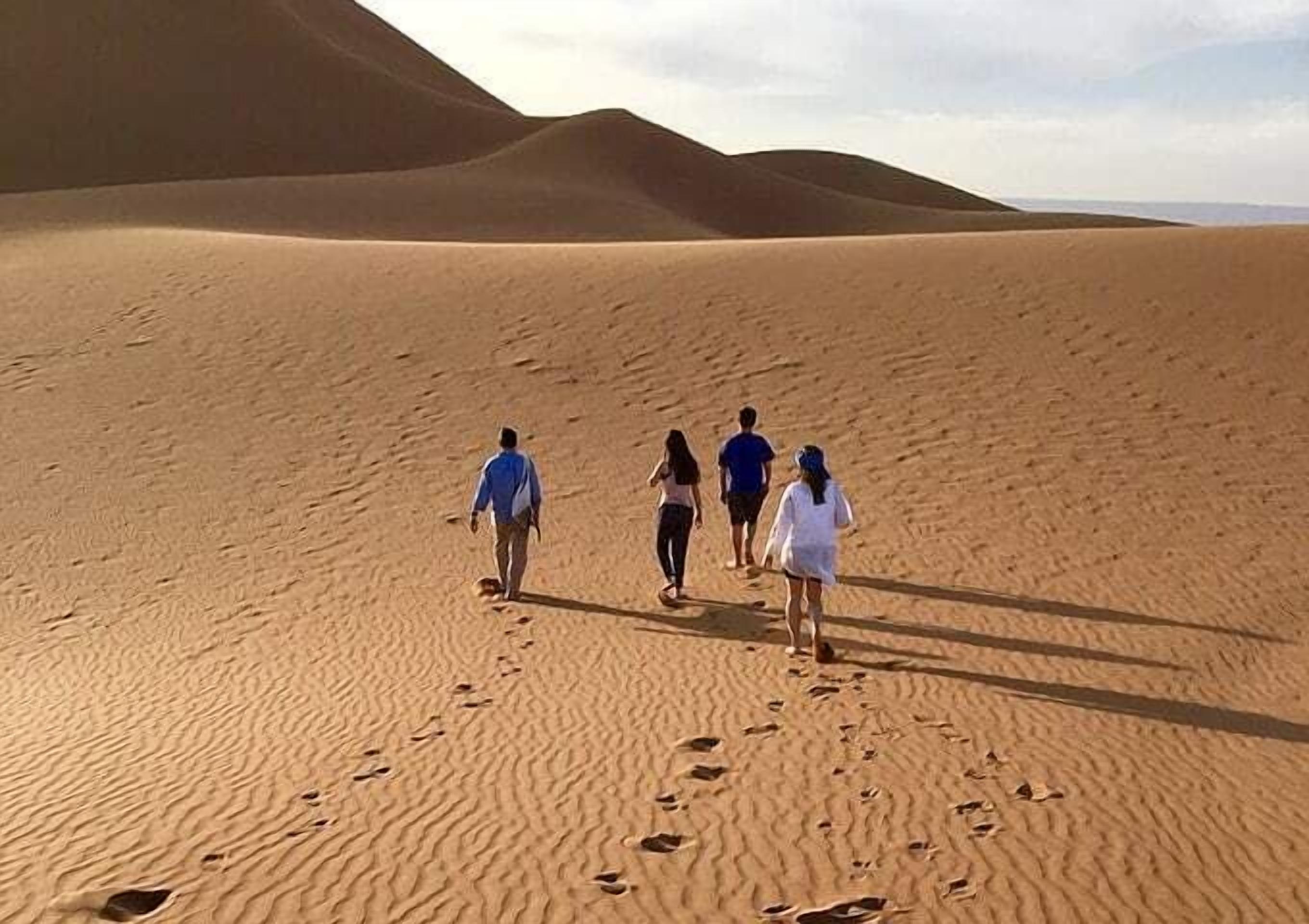 A group of people walking on a sandy desert landscape with dunes in the background.