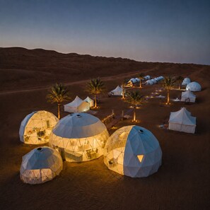 Dome-shaped tents with interior lighting, arranged in a desert setting with palm trees. - Luxury Desert Camp Oman (Bidiya)