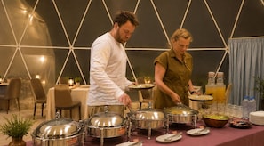 A buffet setup with covered food containers and a table with plates and cutlery. - Luxury Desert Camp Oman (Bidiya)