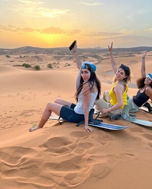Three people sitting on sand dunes with a sunset in the background. - Luxury Desert Camp Oman (Bidiya)