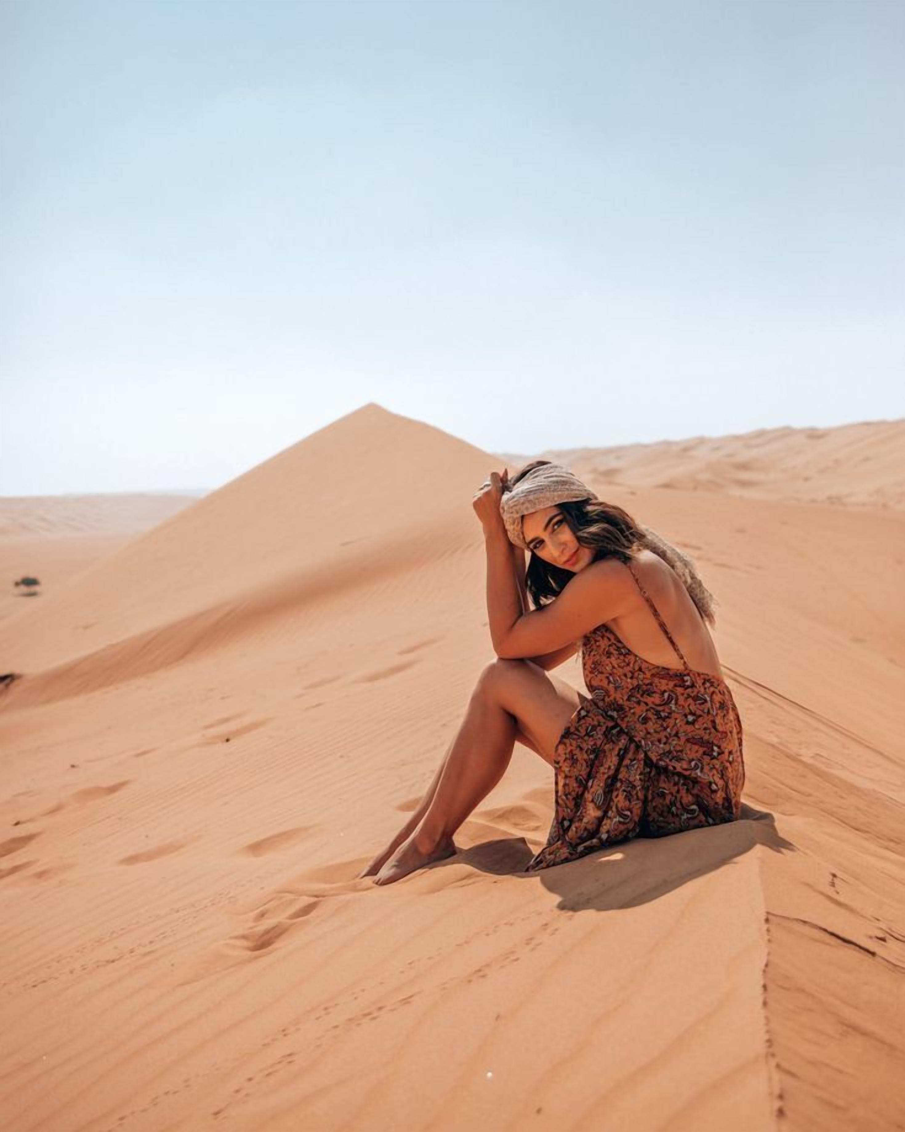 Une personne assise sur une dune de sable dans un paysage désertique.