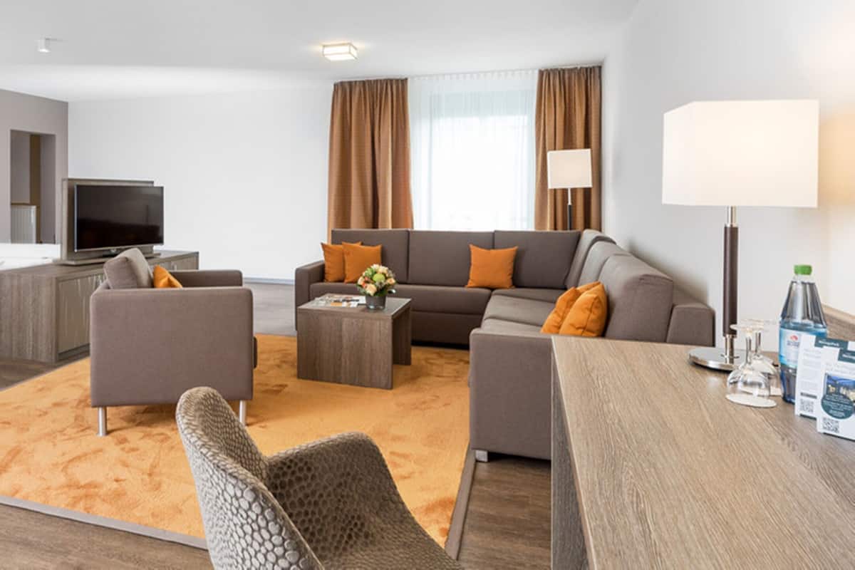 Ein modernes Hotelzimmer mit Bett, Fernseher, Sofa, Couchtisch und Schreibtisch.