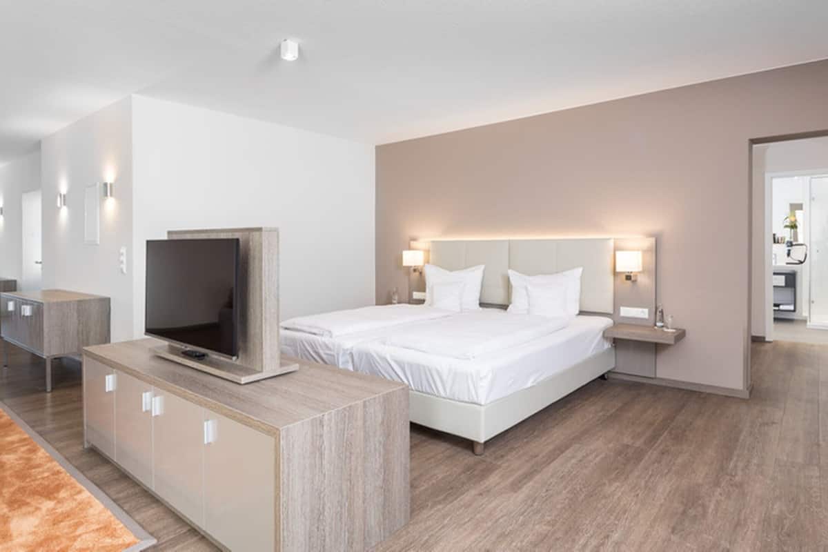 Ein modernes Hotelzimmer mit einem großen Bett, einem Fernseher, einem Schreibtisch und einem durch eine offene Tür einsehbaren Badezimmer.