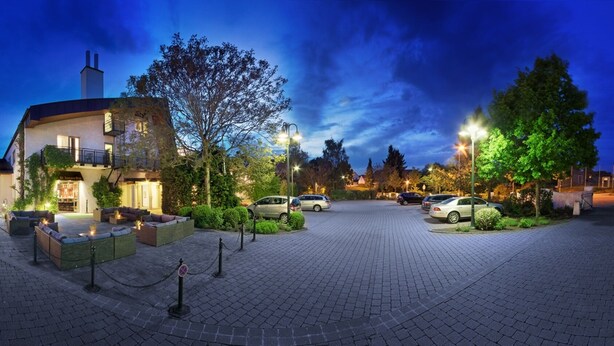 A hotel with a paved courtyard, multiple buildings, and a well-lit entrance. - HerzogsPark Studios & Apartments (Herzogenaurach)