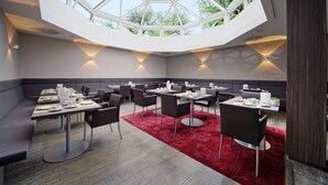 A modern dining area with a high ceiling and skylight, featuring tables and chairs arranged for dining. - HerzogsPark Studios & Apartments (Herzogenaurach)