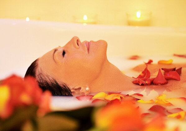 A person lying in a bathtub surrounded by rose petals.